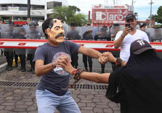 Protestující nosí výsměchovou masku Daniel Ortega