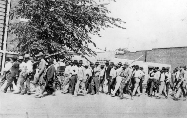 Skupina vojáků Národní gardy s puškami s připojenými bajonety eskortuje neozbrojené černochy do zadržovacího centra po rasovém masakru v Tulse v Tulse v Oklahomě v červnu 1921.