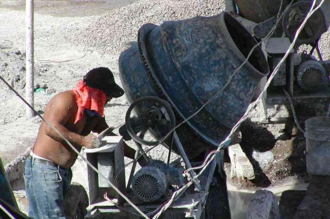 muž v džínách bez košile, červený šátek pod kloboukem, pracuje malý, kulatý stroj na míchání cementu