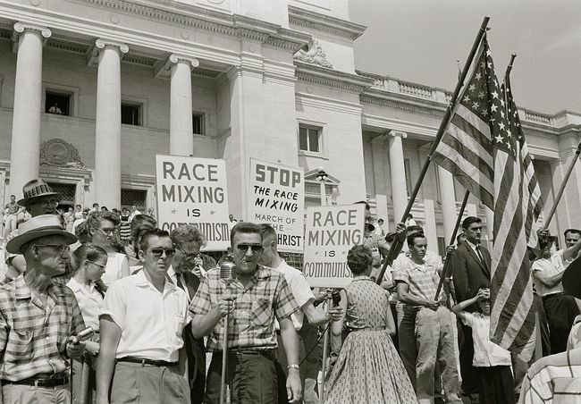 Lidé držící nápisy a americké vlajky protestující proti přijetí „Little Rock Nine“ na střední střední školu.