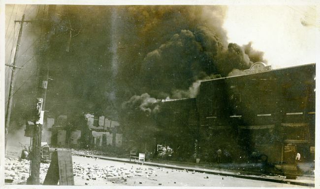 Poškozené nemovitosti a kouř vycházející z budov po masakru v Tulse Race, Tulsa, Oklahoma, červen 1921.