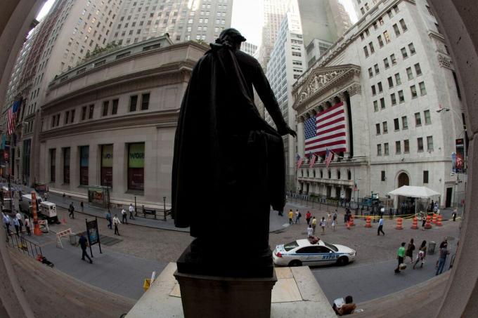 Za obrovskou americkou vlajkou pokrývající kolonádu je fasáda burzy v New Yorku sledována sochou George Washingtona na Wall Street.