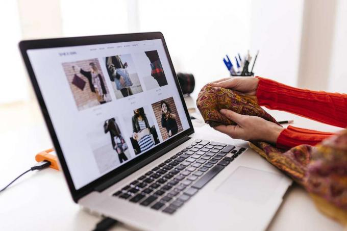 Žena drží látku před notebookem s otevřenou webovou stránkou módy