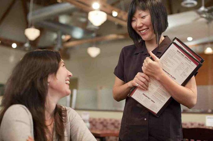 Servírka s menu v ruce mluví se zákazníkem.