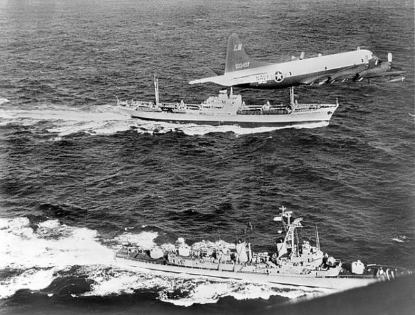 Sovětská nákladní loď Anosov, vzadu, je doprovázena letadlem námořnictva a torpédoborcem USS Barry, zatímco opouští Kubu během kubánské raketové krize v roce 1962.