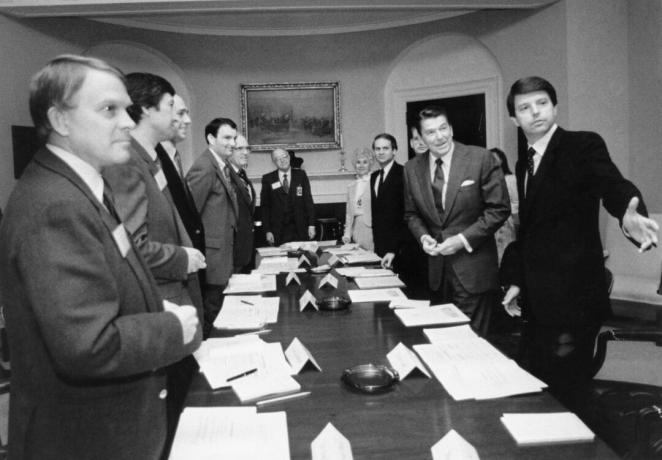 Černobílý obraz Ronalda Reagana a několika dalších mužů v oblecích kolem dlouhého konferenčního stolu