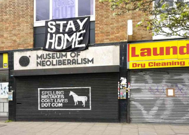 Velká značka STAY HOME výše uzavřené Muzeum neoliberalismu v Lewsihamu v Londýně, Anglie.